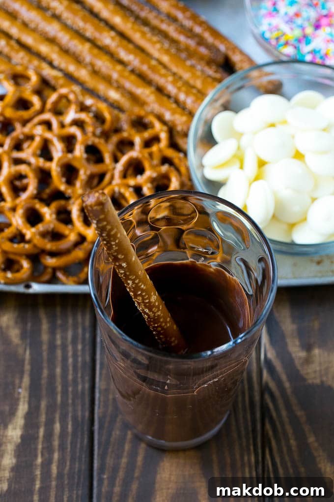 Chocolate Covered Pretzels Recipe | Sprinkle Pretzels | No Bake Dessert #pretzels #chocolate #christmas #sprinkles #candy #dinneratthezoo A rod in a glass full of melted chocolate.