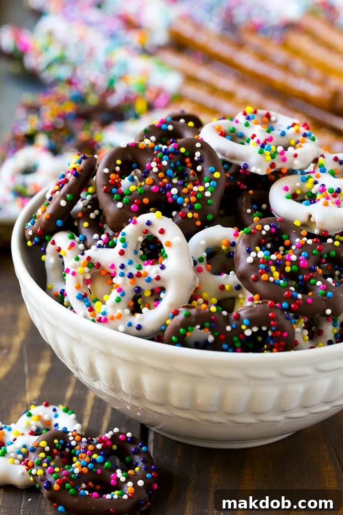 Chocolate Covered Pretzels Recipe | Sprinkle Pretzels | No Bake Dessert #pretzels #chocolate #christmas #sprinkles #candy #dinneratthezoo A bowl of chocolate covered pretzels decorated with rainbow sprinkles.