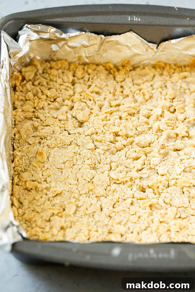 Brown Sugar Oatmeal Crust for Peach Bars A close-up view of the oatmeal and brown sugar crust, perfectly pressed into a baking pan, forming the foundational layer of the peach crumble bars.