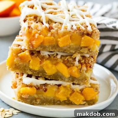 Peach Crumble Bars - Recipe Image A stack of peach crumble bars topped with vanilla glaze, cut into neat squares, displaying their inviting layers.