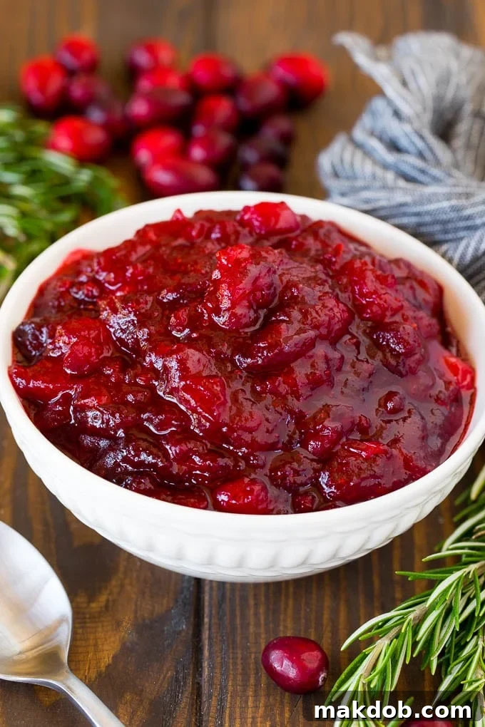 Discover the best homemade cranberry sauce, a vibrant and flavorful accompaniment to any holiday feast, made with fresh cranberries, sugar, and warming spices. A beautifully presented bowl of homemade cranberry sauce, garnished with fresh cranberries and a sprig of rosemary, ready to be served with a silver spoon.