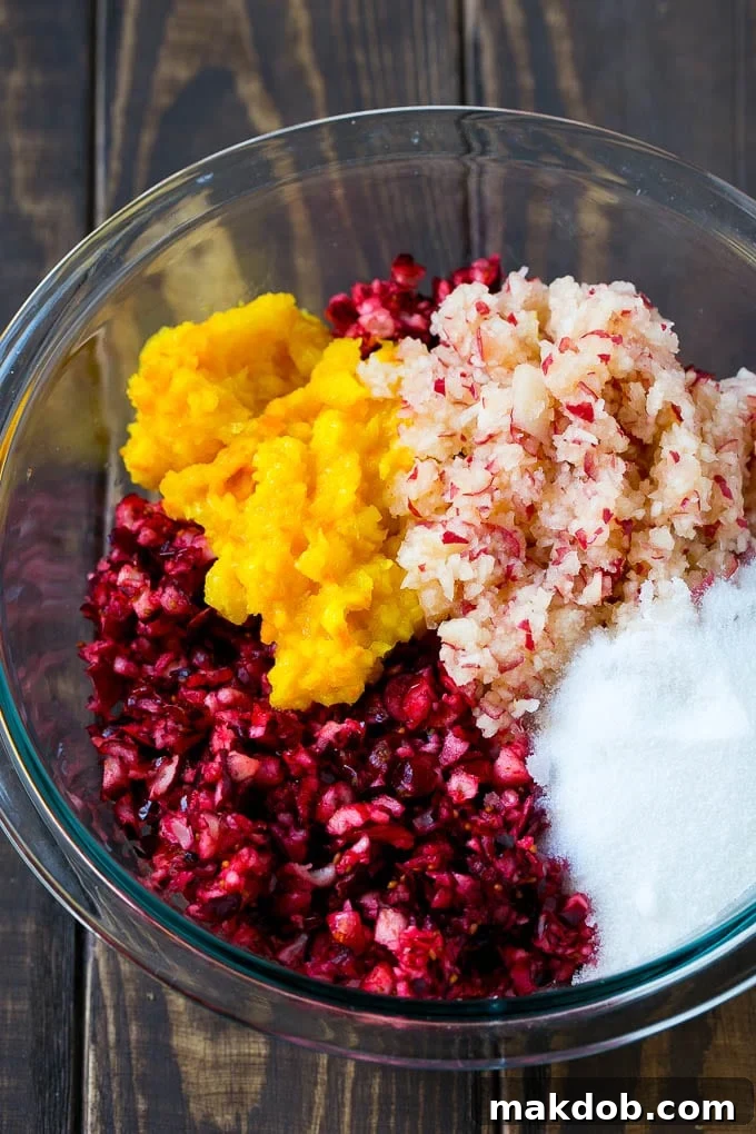 Chopped cranberries, apple and orange with sugar in a mixing bowl, ready to be stirred and chilled.