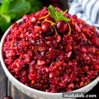 A bowl of cranberry relish topped with whole cranberries, orange zest and mint.