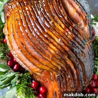 A glazed ham on a platter with herbs and cranberries.