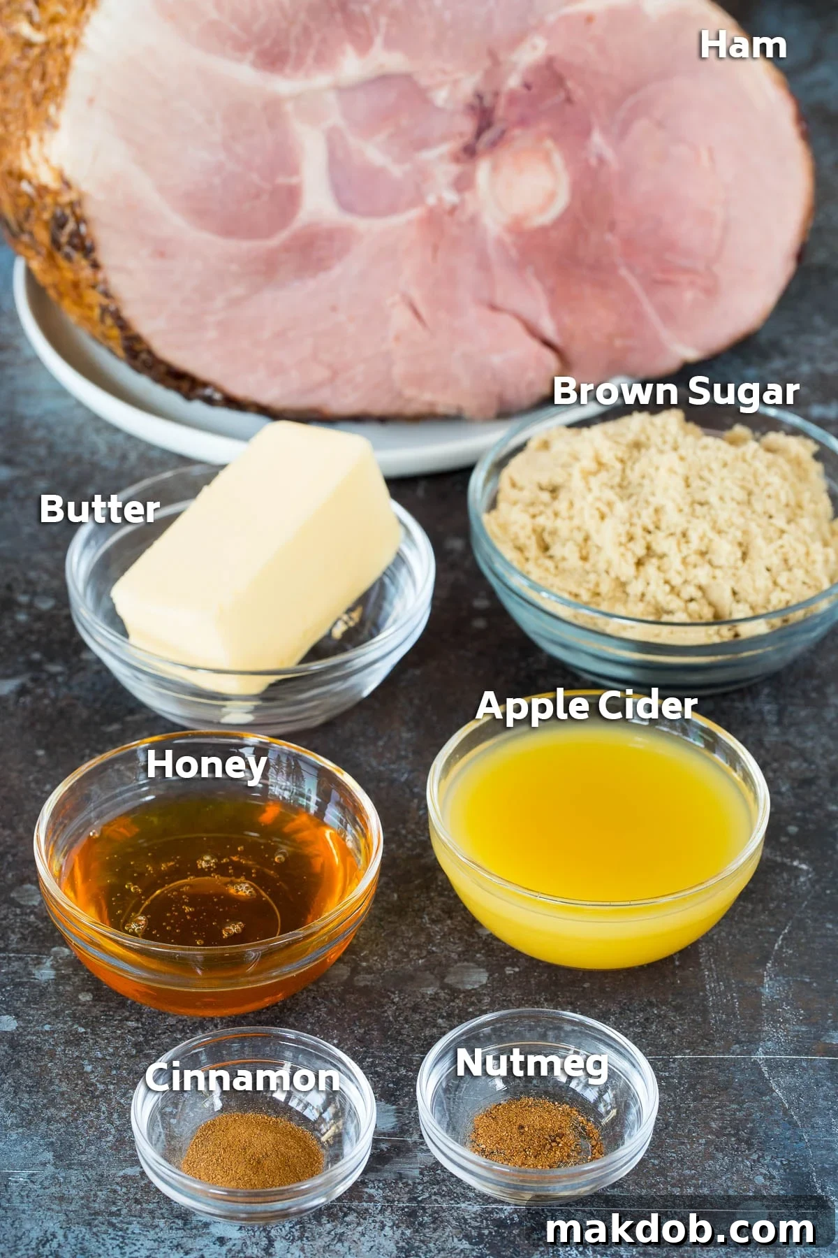 Bowls of essential ingredients for glazed ham including butter, brown sugar, honey, apple cider, cinnamon, and nutmeg.