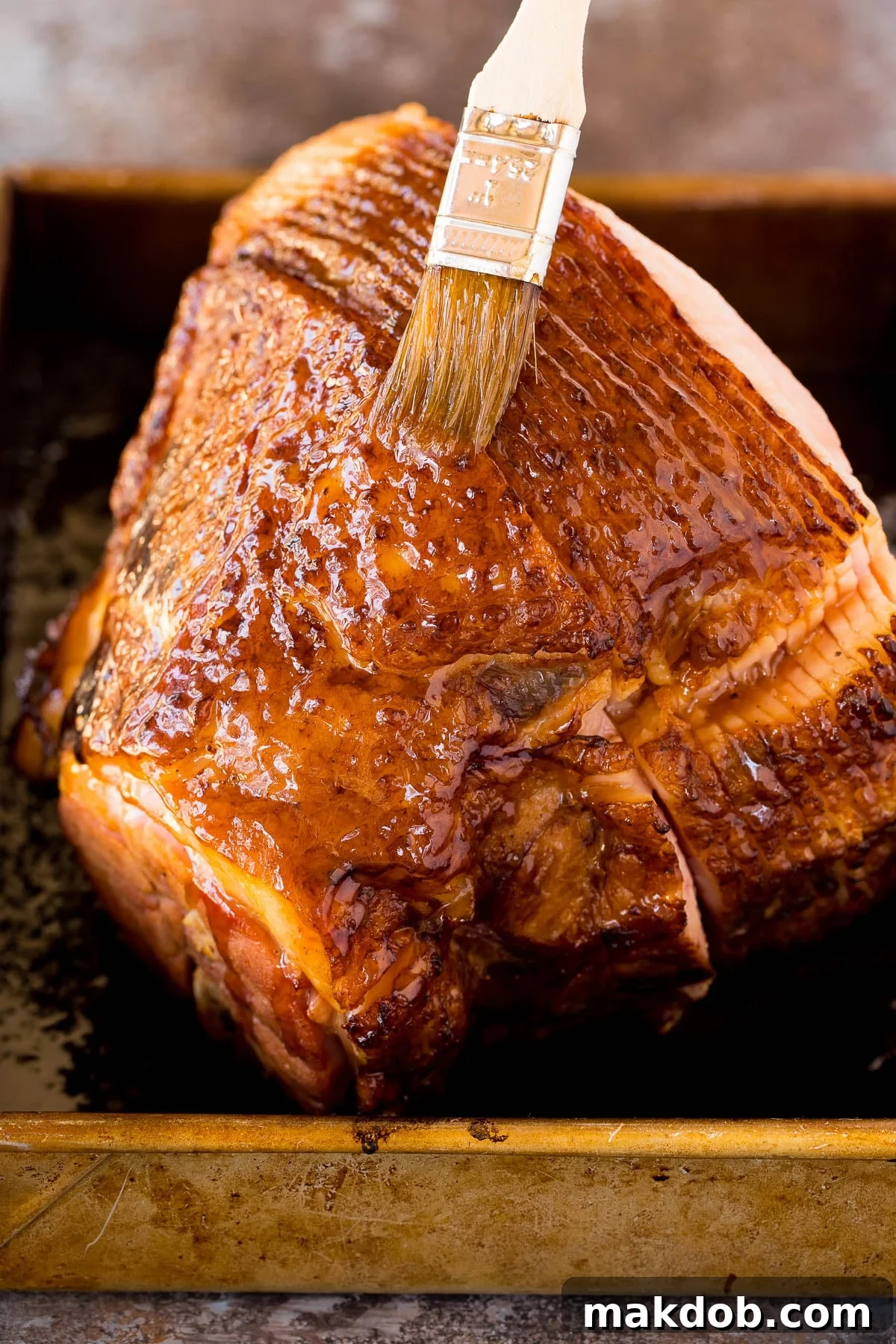 A basting brush applying the sweet brown sugar and honey glaze to the baking ham, ensuring even coverage.