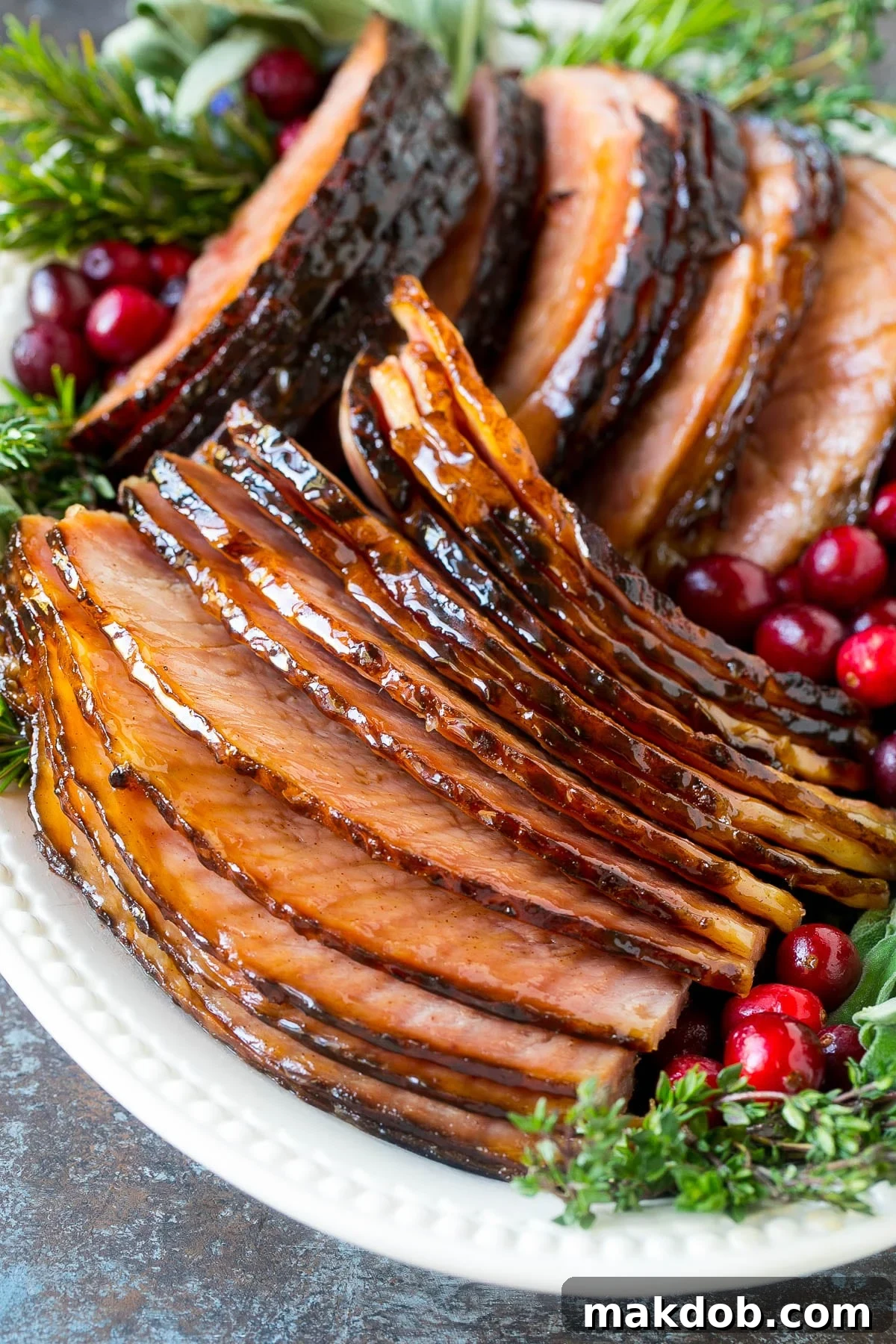 Close-up of perfectly sliced glazed ham on a serving plate, adorned with vibrant berries and fresh herbs.