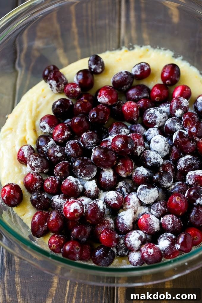 Orange batter topped with a pile of fresh cranberries in a mixing bowl, ready to be folded in.