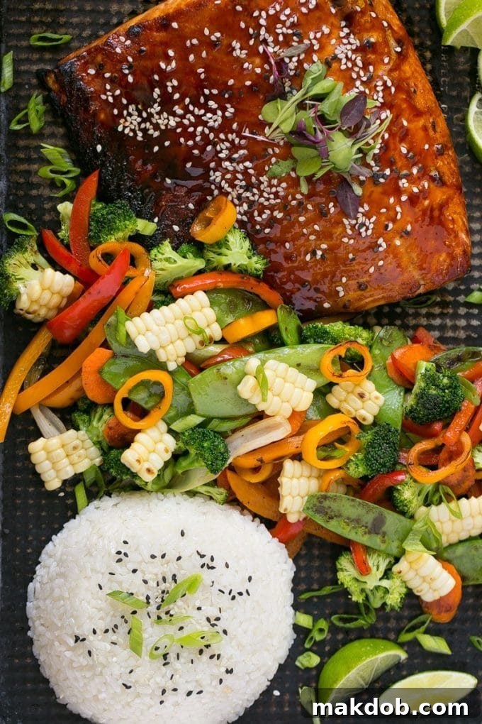 A sheet pan showcasing hoisin glazed salmon, perfectly roasted mixed vegetables, accompanied by a bowl of steamed rice.