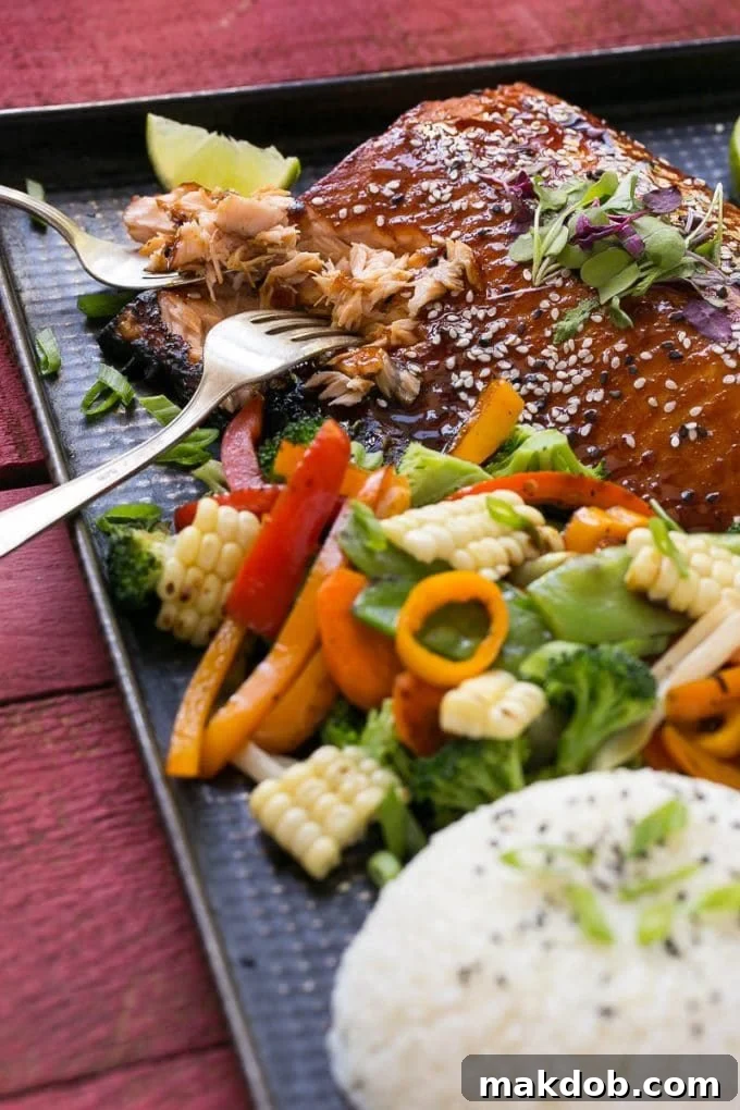 Two forks delicately separating a flaky piece of perfectly cooked Asian salmon, highlighting its tender texture.