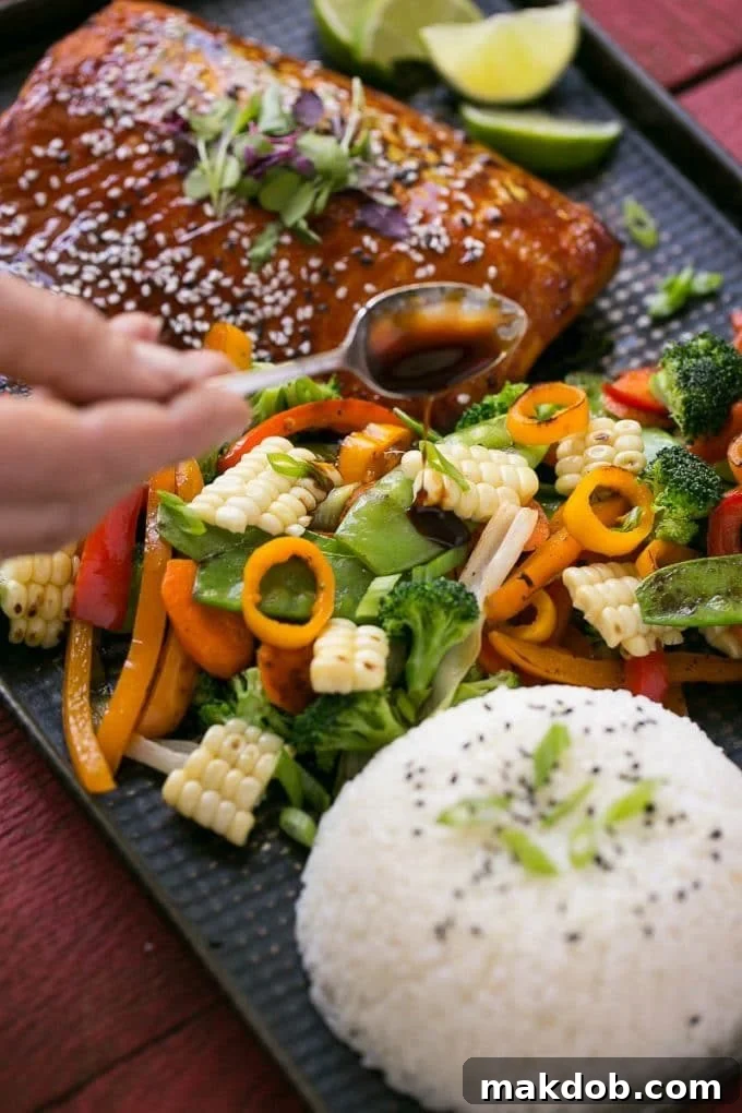 A close-up shot of a spoonful of glossy hoisin lime glaze being poured over a vibrant mix of cooked vegetables.