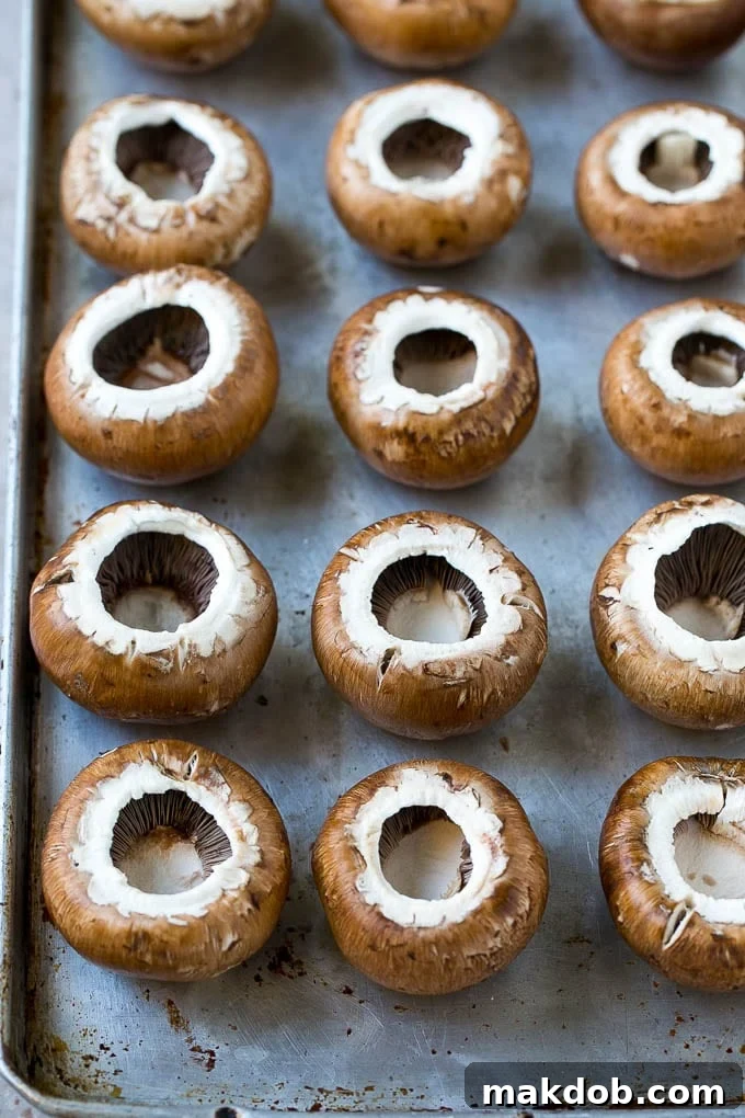 Cremini mushroom caps neatly arranged on a sheet pan, ready for stuffing.