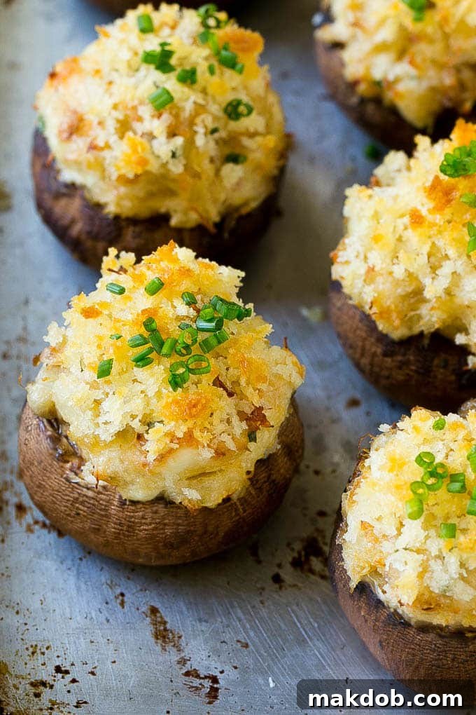 Baked crab stuffed mushrooms garnished with freshly sliced chives on a sheet pan.