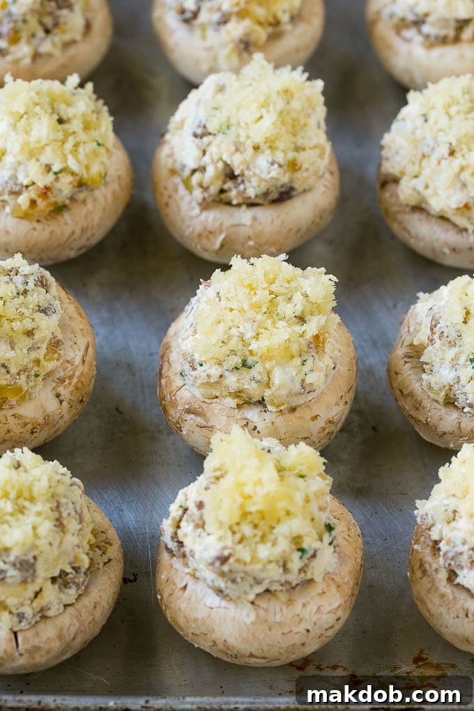 Raw sausage stuffed mushrooms arranged on a baking sheet, glistening and ready to go into the hot oven.