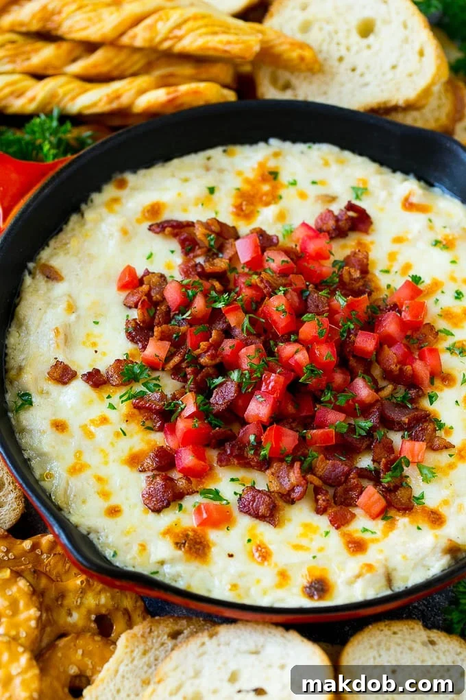Baked chicken Alfredo dip in a skillet topped with bacon, tomatoes and chopped parsley.