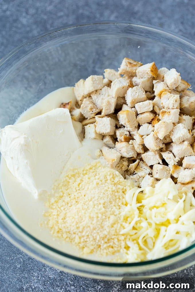Chicken, Alfredo sauce, cream cheese, mozzarella and parmesan cheese in a mixing bowl.