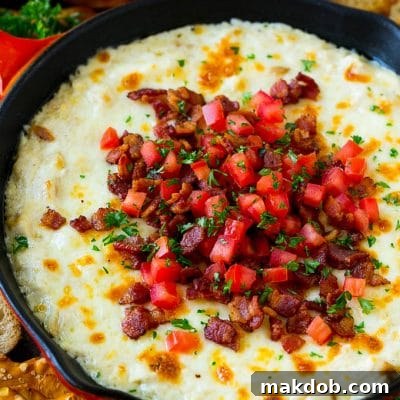 Baked chicken Alfredo dip in a skillet topped with bacon, tomatoes and chopped parsley.