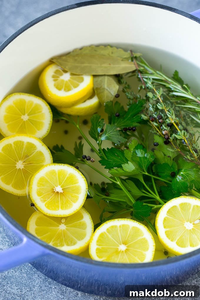 This chicken brine recipe is made with lemons, honey, fresh herbs and spices, and produces a juicy tender chicken every time! A foolproof way for succulent and flavorful roasted, smoked or fried chicken. A large stainless steel pot filled with water, featuring floating lemon slices, whole peppercorns, and fresh herbs, simmering on a stovetop to create the brine solution.