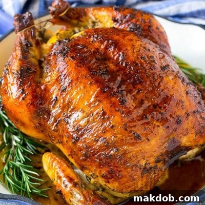 A roasted chicken in a pan garnished with fresh rosemary sprigs.