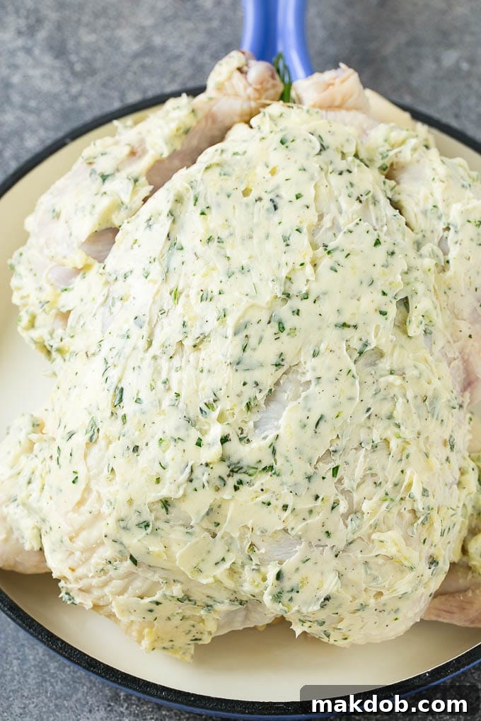 A raw whole chicken coated in garlic and herb butter.