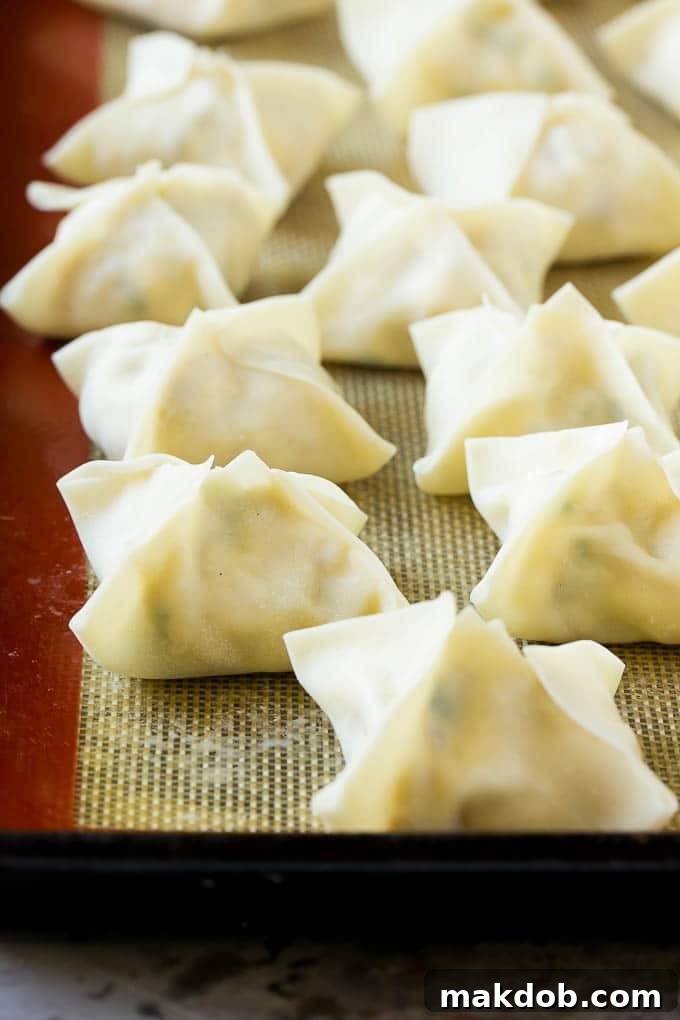Crab Rangoon Recipe | Crab Wontons | Cream Cheese Wontons #crab #cheese #appetizer #snack #chinesefood #dinner #dinneratthezoo Rows of raw, perfectly folded wontons resting on a baking sheet, ready for frying.