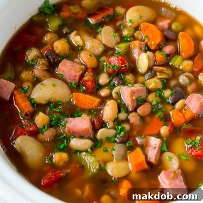 A slow cooker full of ham and bean soup made with vegetables, dried beans and diced ham.