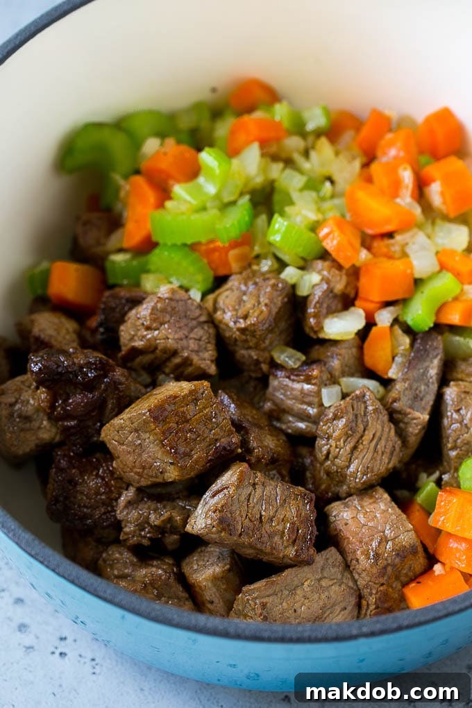 Stew meat, carrots, onions, and celery sautéing together in a large pot, building layers of flavor.