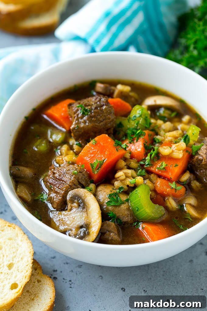 A steaming bowl of beef barley soup, garnished with fresh chopped parsley, ready to be enjoyed.
