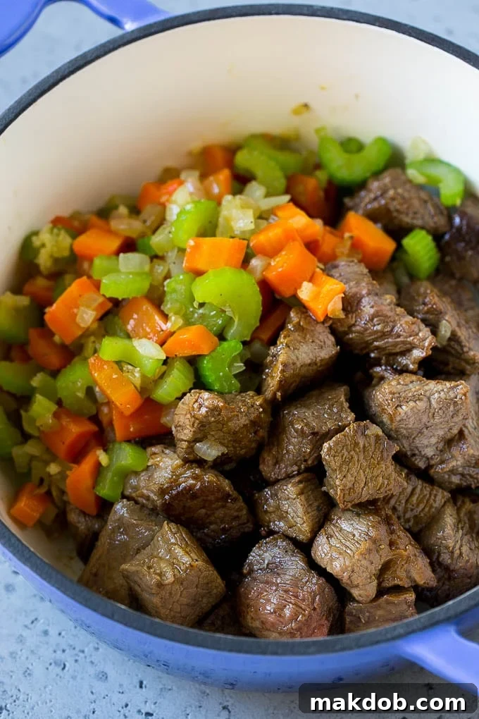 A large pot filled with beef stew meat, carrots, onion, and celery sautéing together, forming the aromatic base for the soup.
