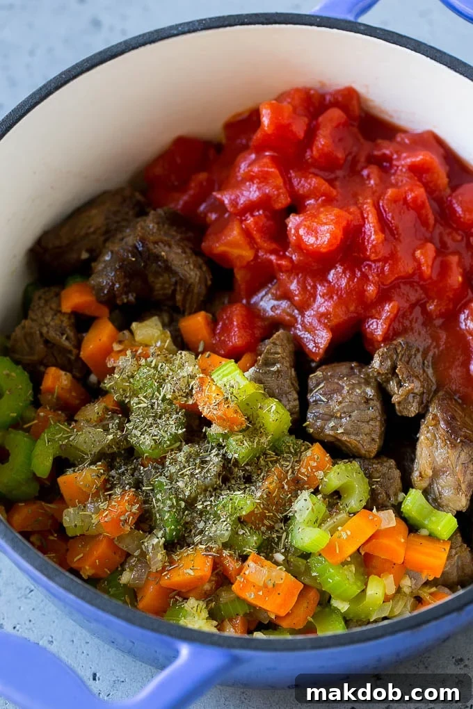 Close-up view of beef stew meat, various vegetables like carrots, celery, and onions, diced tomatoes, and herbs simmering together in a large pot, creating a rich and aromatic broth.