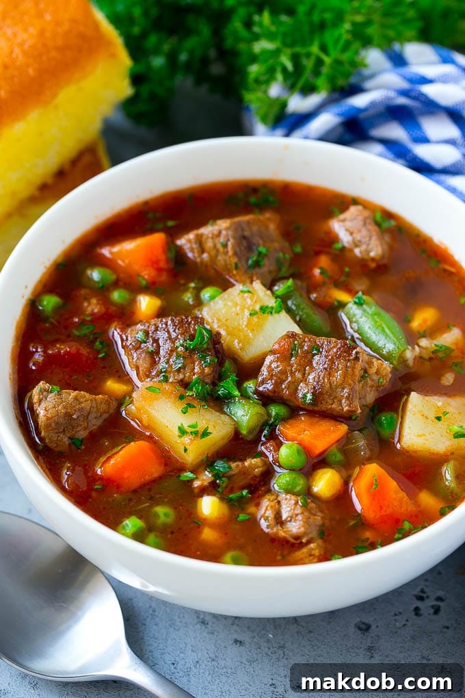 A beautifully presented bowl of vegetable beef soup, garnished with fresh parsley, highlighting carrots, celery, onions, potatoes, tomatoes, corn, and peas.