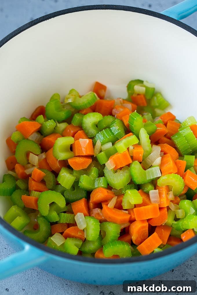 Finely chopped celery, carrots, and onion simmering in a large soup pot, forming the aromatic base for chicken and rice soup.
