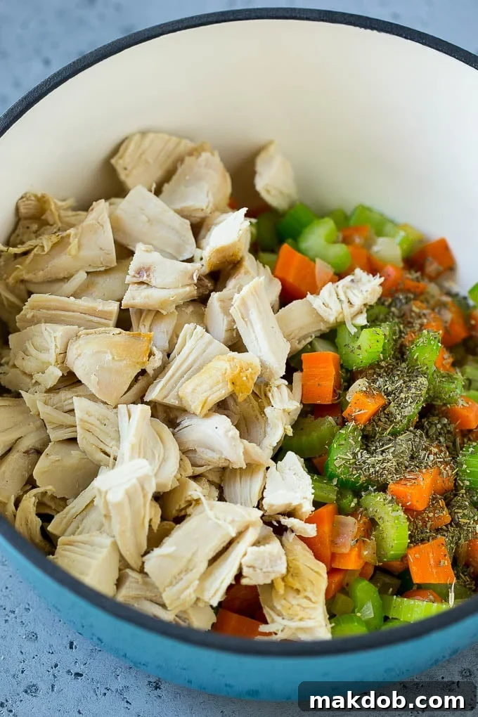 Shredded cooked chicken, dried herbs like Italian seasoning, and the already sautéed vegetables in a large soup pot, ready for broth.