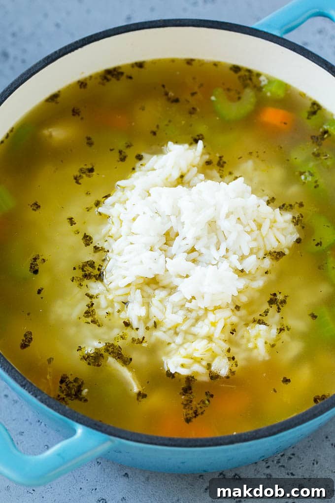 Cooked rice being stirred into a rich pot of chicken and vegetable soup, creating a hearty and comforting meal.