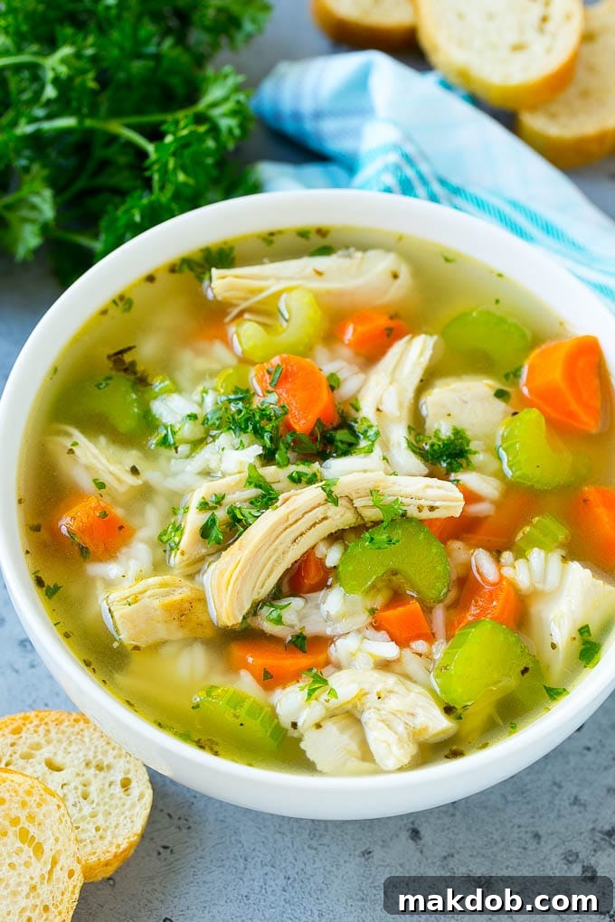 A hearty bowl of chicken and rice soup, generously garnished with fresh chopped parsley leaves, showcasing tender chicken, vegetables, and rice.