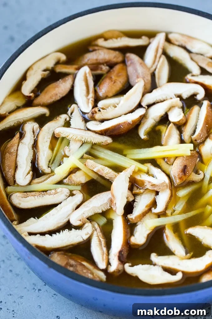 A close-up of sliced shiitake mushrooms and bamboo shoots simmering in a clear, savory broth, highlighting the fresh, earthy ingredients that form the base of an authentic Hot and Sour Soup.