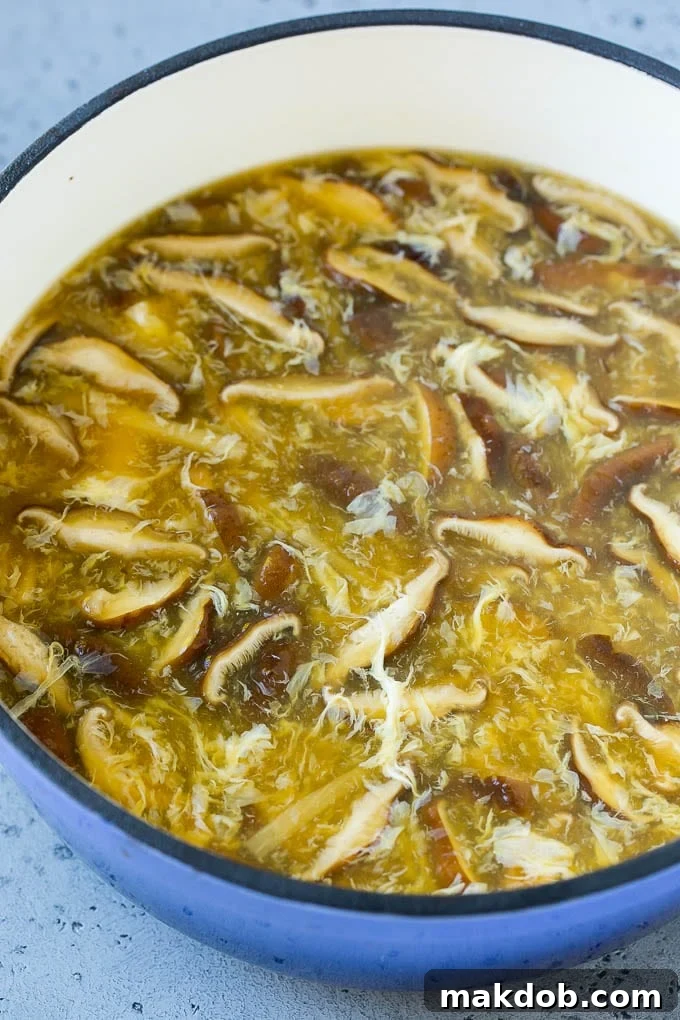 A close-up shot of a pot of Hot and Sour Soup in progress, showing the delightful combination of mushrooms, tender egg strands, and crisp bamboo shoots swirling in the rich broth, promising a flavorful meal.