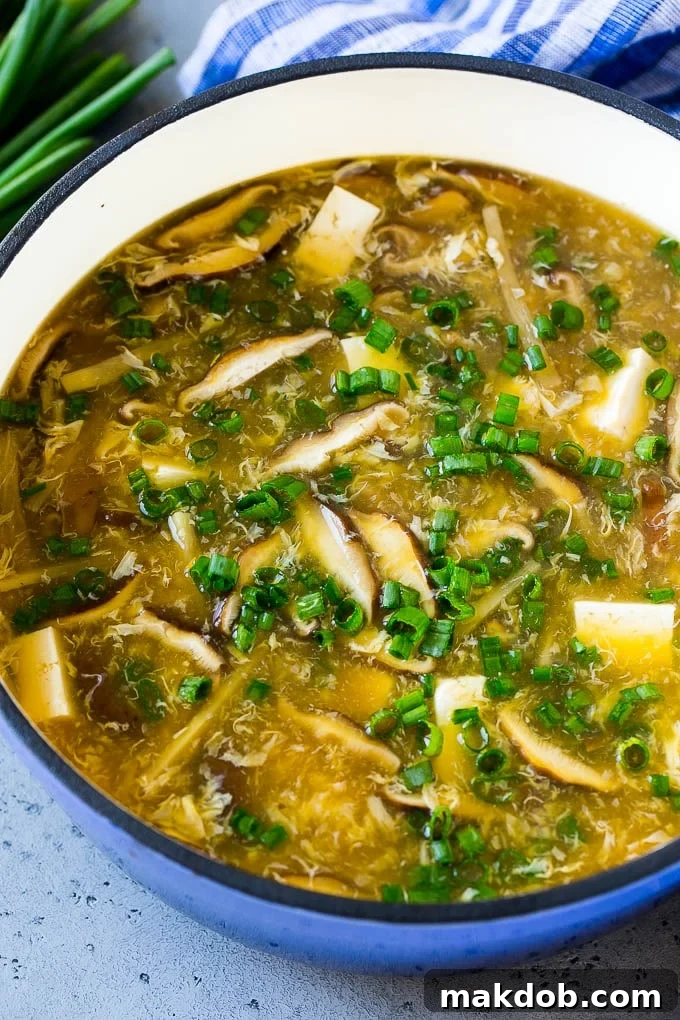 A large pot of freshly made homemade Hot and Sour Soup, filled with an abundance of shiitake mushrooms, tender tofu, crisp bamboo shoots, delicate egg strands, and bright green onions, ready to be served and enjoyed as a comforting and flavorful dish.