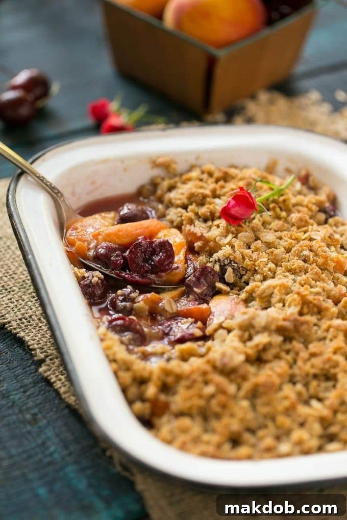 A serving spoon lifting a scoop of bubbly fruit crisp from a baking dish, showcasing its golden-brown topping and vibrant fruit filling.