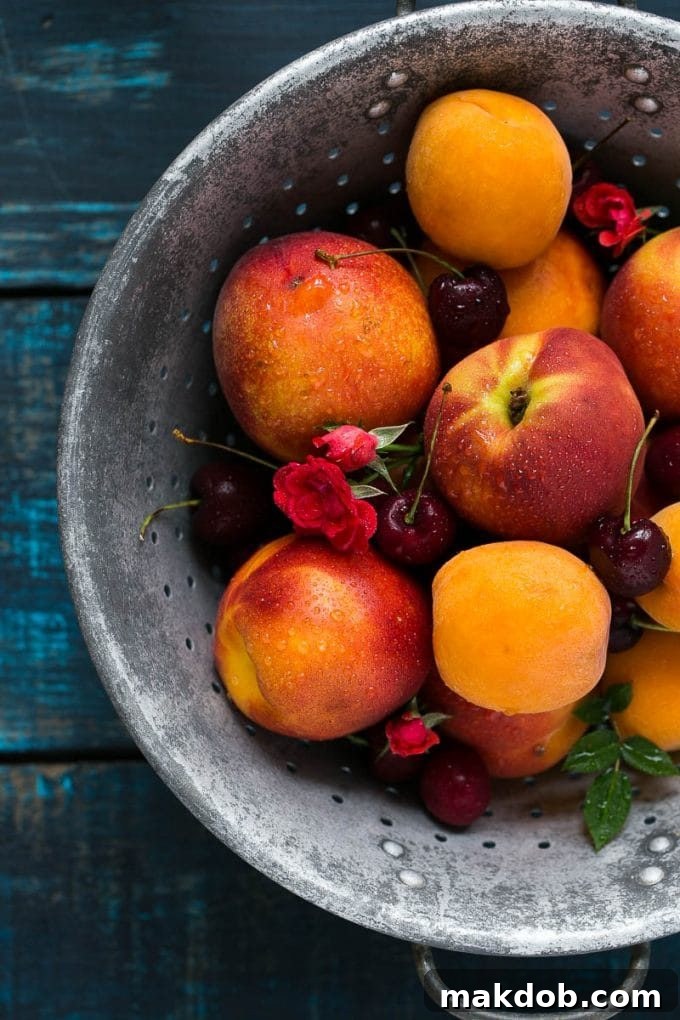 A vibrant colander overflowing with freshly washed peaches, apricots, and dark red cherries, ready for a delicious fruit crisp.