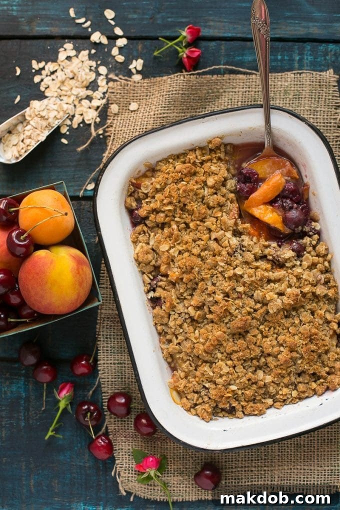 A close-up shot of a baking pan filled with a bubbling cherry and peach crisp, topped with a golden, crumbly oatmeal mixture.