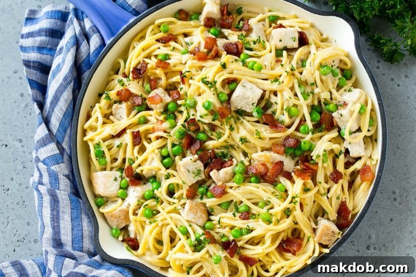 An appetizing close-up of a pan filled with turkey carbonara pasta, featuring generous pieces of bacon, bright green peas, and fresh parsley, all glistening in a creamy sauce.