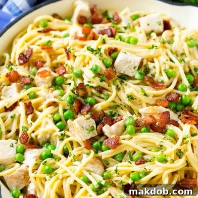 A skillet of turkey pasta carbonara with peas and bacon in a creamy sauce.