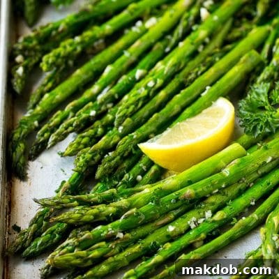 Roasted asparagus on a sheet pan, topped with chopped parsley and garnished with lemon wedges.