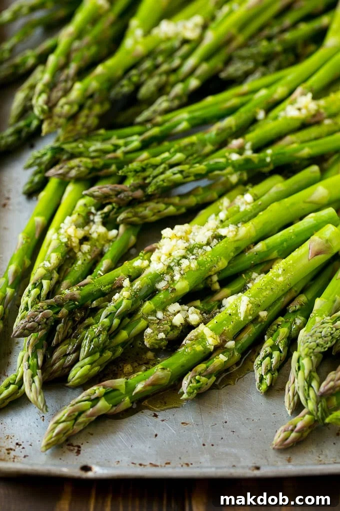 Raw asparagus spears drizzled with olive oil, garlic, herbs, salt and pepper on a baking sheet.