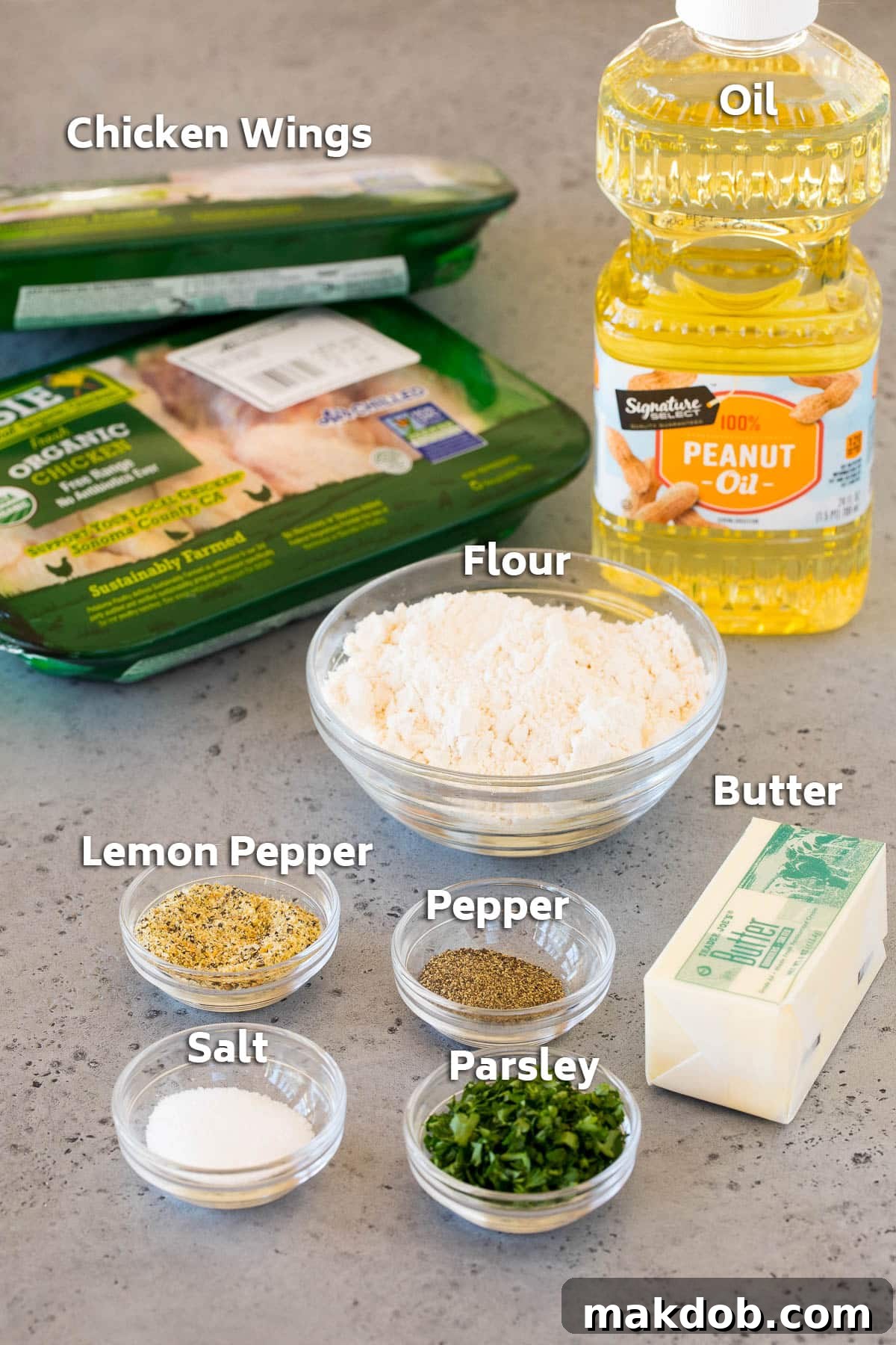 Citrus Peppered Wings 3 A flat lay of fresh ingredients laid out for making lemon pepper wings, including raw chicken wings, butter, flour, salt, pepper, and a bottle of lemon pepper seasoning.