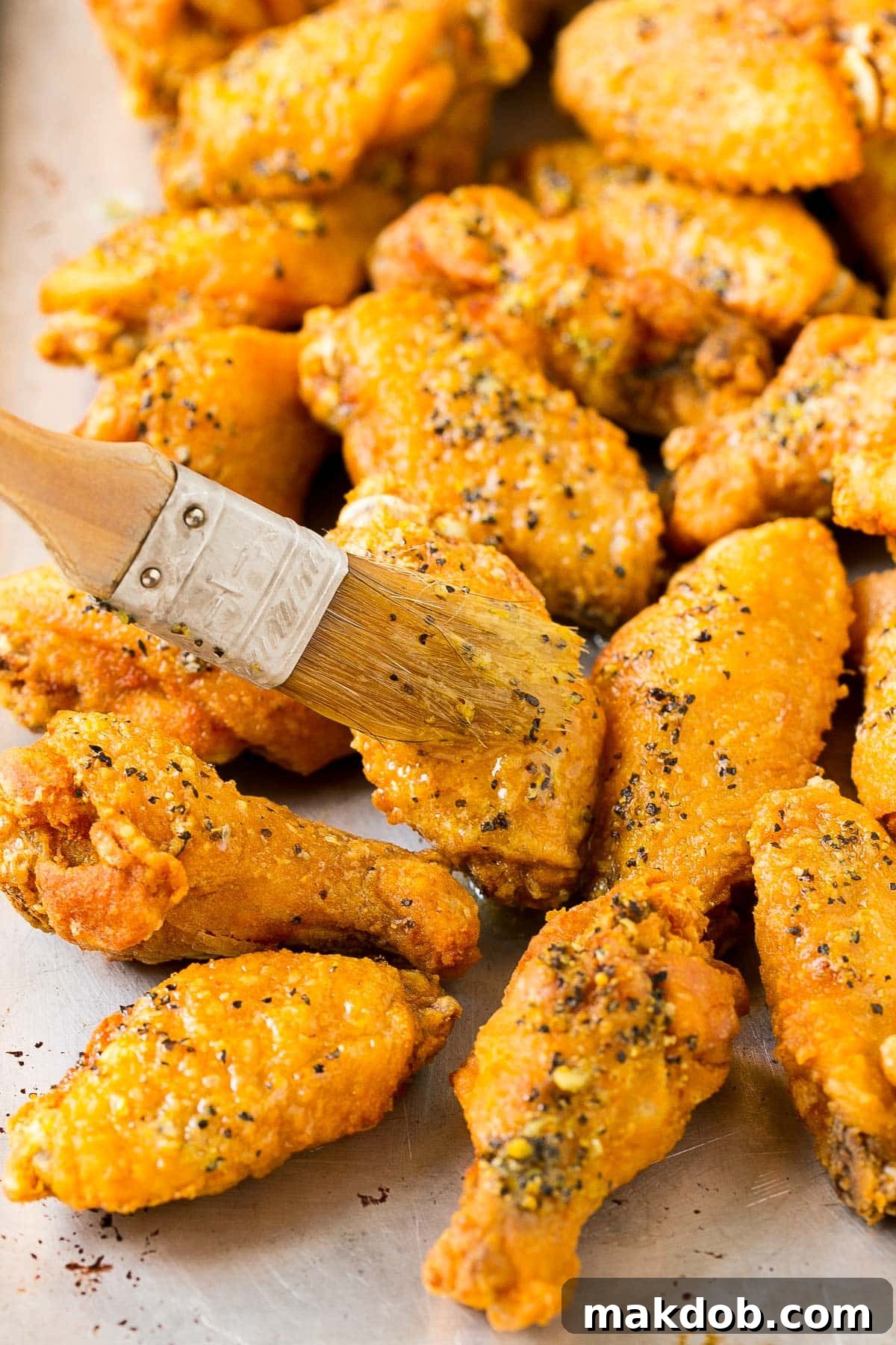 Citrus Peppered Wings 5 A close-up shot of a pastry brush applying seasoned butter onto freshly fried chicken wings, creating a glistening, flavorful coating.