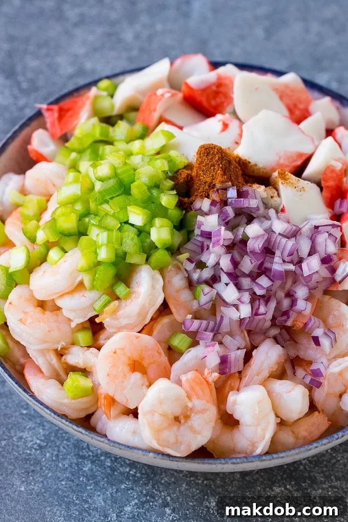 Shrimp, imitation crab, red onion, celery and Old Bay seasoning in a bowl.
