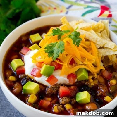 A bowl of taco soup topped with tortilla strips, sour cream, cheese and avocado.