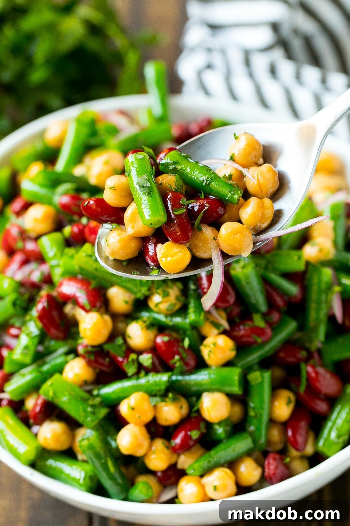 A spoon lifting a serving of three bean salad from a large bowl, showing the individual beans and dressing.